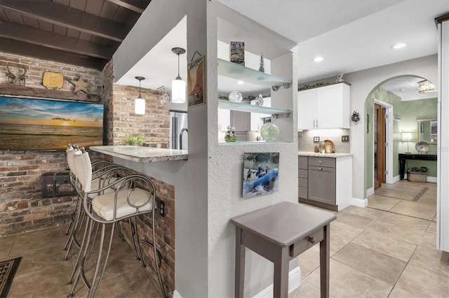 kitchen with light tile patterned floors, arched walkways, brick wall, a breakfast bar, and open shelves