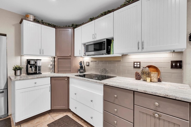 kitchen with light tile patterned floors, white cabinetry, appliances with stainless steel finishes, decorative backsplash, and light stone countertops