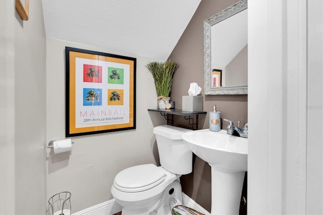 half bathroom with lofted ceiling, a textured ceiling, toilet, a sink, and baseboards