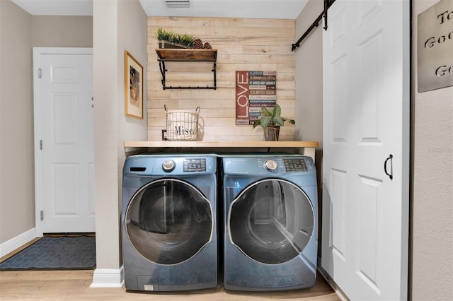 laundry room with a barn door, wood walls, separate washer and dryer, wood finished floors, and baseboards