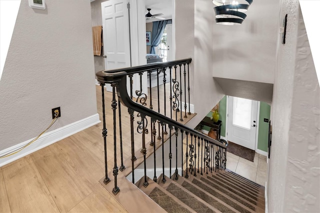 stairway featuring ceiling fan, a textured wall, wood finished floors, and baseboards