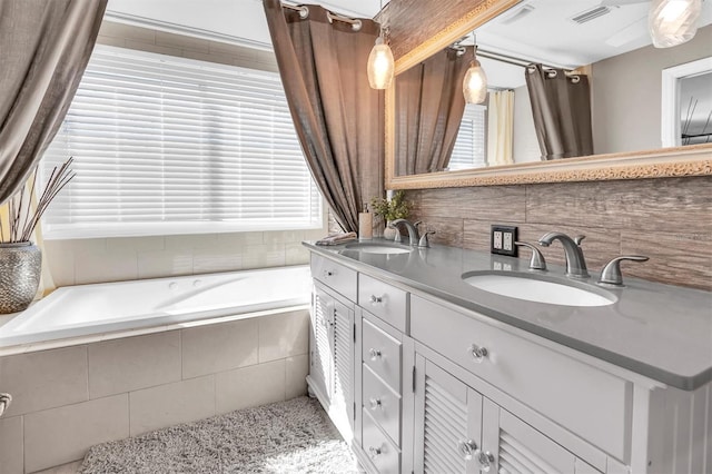 bathroom with decorative backsplash, visible vents, a sink, and a garden tub