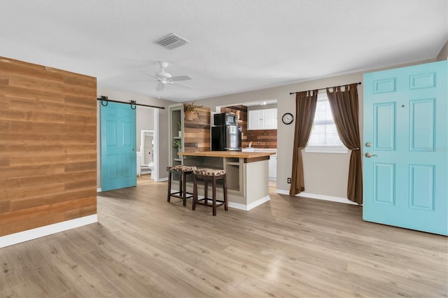 kitchen with a breakfast bar area, visible vents, a barn door, light wood-style floors, and white cabinets