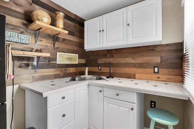 kitchen with wood walls, tile counters, white cabinets, and a sink