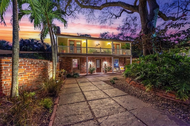 back of property at dusk with a balcony, french doors, and brick siding