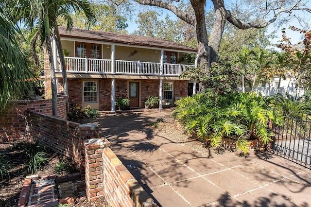 view of front of house featuring brick siding, fence, a balcony, and stucco siding