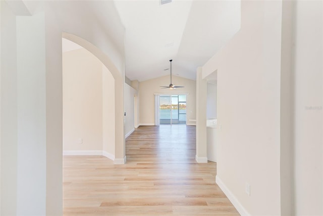 corridor with light wood-type flooring, baseboards, vaulted ceiling, and arched walkways