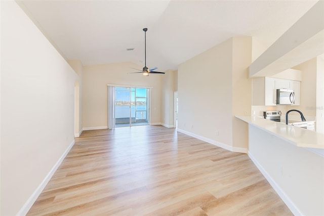 empty room featuring baseboards, a ceiling fan, vaulted ceiling, light wood-type flooring, and a sink