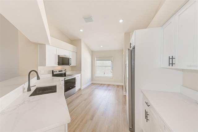 kitchen with white cabinets, light stone countertops, stainless steel appliances, light wood-type flooring, and a sink