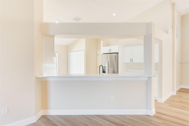 kitchen with stainless steel refrigerator with ice dispenser, lofted ceiling, light countertops, white cabinetry, and light wood-type flooring