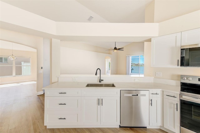 kitchen with appliances with stainless steel finishes, light wood-style floors, white cabinetry, a sink, and a peninsula