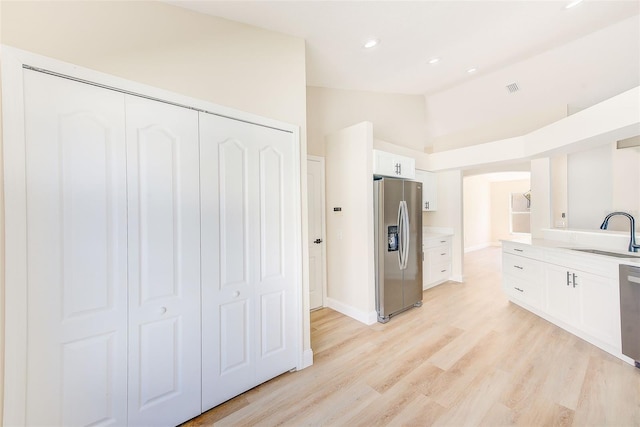 kitchen featuring lofted ceiling, light wood-style flooring, appliances with stainless steel finishes, white cabinets, and a sink