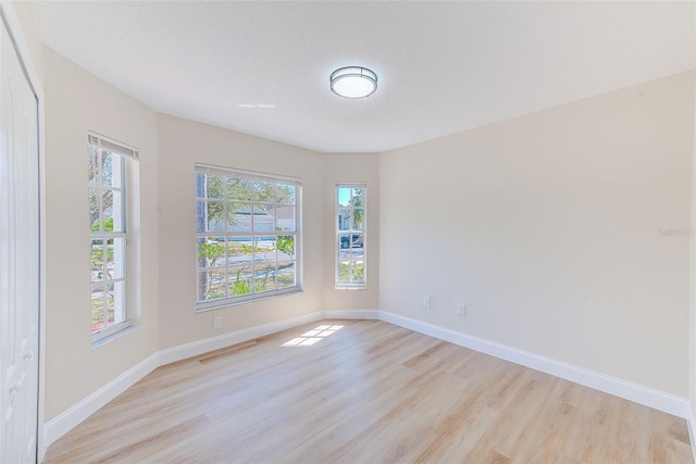 empty room featuring a textured ceiling, light wood-type flooring, and baseboards