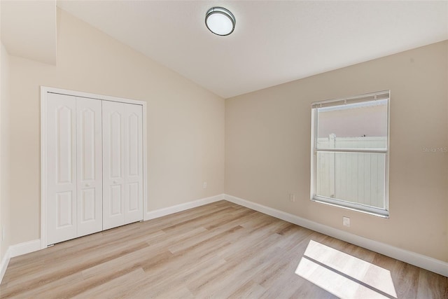 unfurnished bedroom featuring vaulted ceiling, a closet, wood finished floors, and baseboards