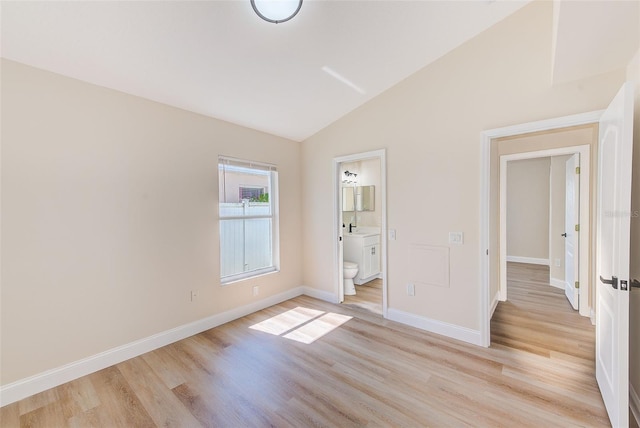 unfurnished bedroom featuring connected bathroom, baseboards, vaulted ceiling, and light wood finished floors