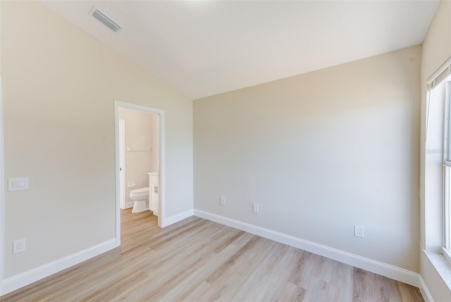 empty room featuring vaulted ceiling, light wood-type flooring, visible vents, and baseboards