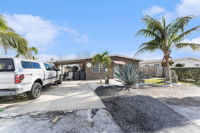 view of front of house featuring a carport, stucco siding, driveway, and fence