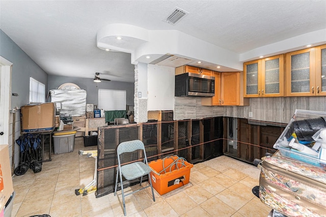 kitchen featuring light tile patterned floors, visible vents, ceiling fan, glass insert cabinets, and stainless steel microwave