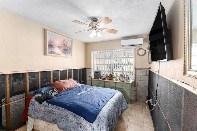 bedroom featuring a wall unit AC, light tile patterned floors, wainscoting, ceiling fan, and a textured ceiling