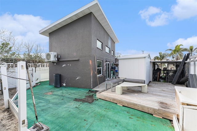 rear view of house featuring an outdoor structure, fence, a wooden deck, stucco siding, and a storage unit