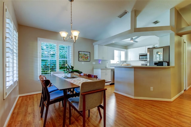 dining area with light wood-style flooring, baseboards, vaulted ceiling, and visible vents
