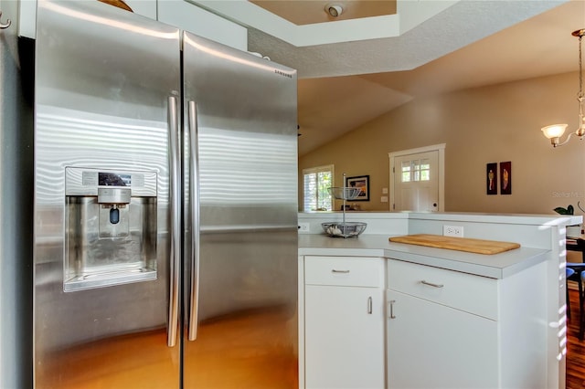 kitchen featuring stainless steel fridge, light countertops, a peninsula, white cabinetry, and vaulted ceiling