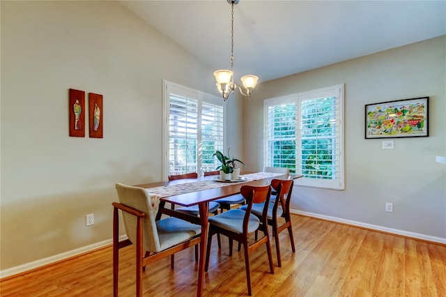 dining area with light wood finished floors, baseboards, an inviting chandelier, and lofted ceiling
