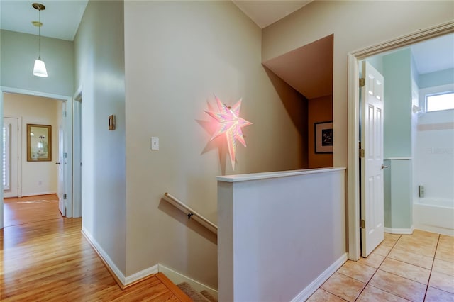 hallway with light tile patterned floors, baseboards, and an upstairs landing