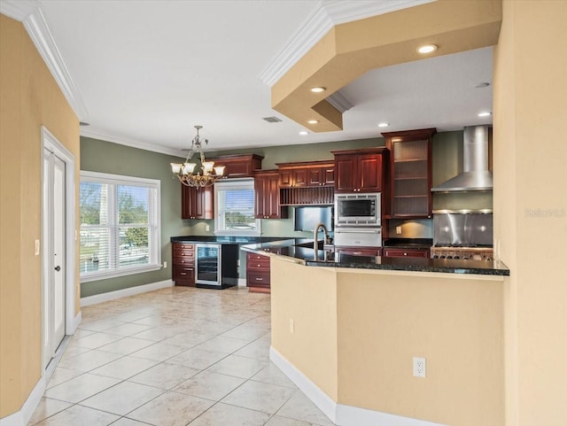 kitchen with reddish brown cabinets, stainless steel microwave, ornamental molding, beverage cooler, and wall chimney exhaust hood