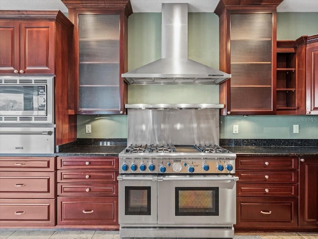 kitchen featuring a warming drawer, appliances with stainless steel finishes, wall chimney range hood, dark brown cabinets, and dark stone counters