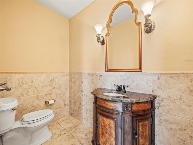 half bath with toilet, tile walls, vanity, wainscoting, and tile patterned floors