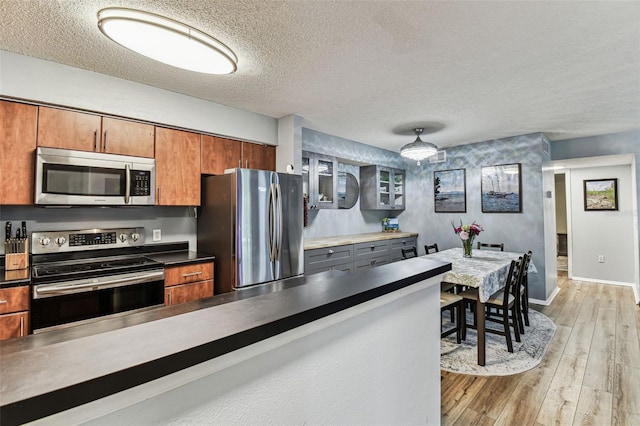 kitchen featuring a textured ceiling, light wood-style flooring, stainless steel appliances, baseboards, and glass insert cabinets