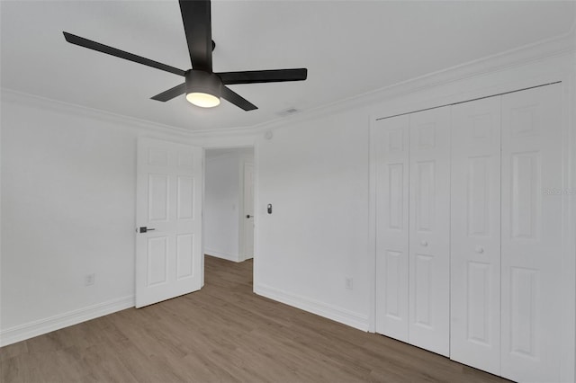 unfurnished bedroom featuring a closet, crown molding, baseboards, and wood finished floors