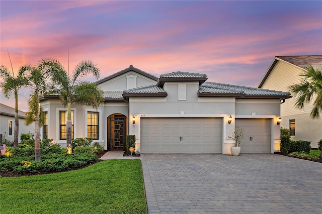 mediterranean / spanish house with a garage, a front lawn, decorative driveway, and stucco siding