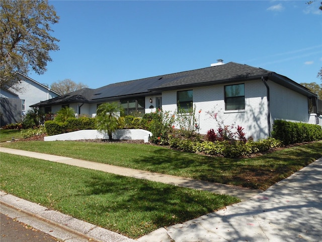 ranch-style home featuring brick siding, roof with shingles, and a front yard