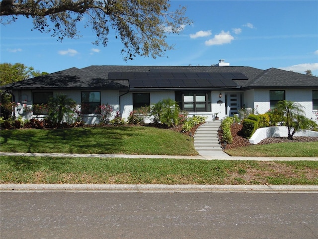 view of front of house featuring brick siding, solar panels, and a front yard