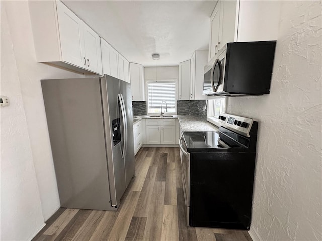 kitchen with stainless steel appliances, a textured wall, white cabinetry, a sink, and wood finished floors