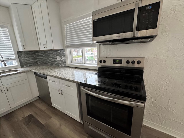 kitchen featuring stainless steel appliances, white cabinetry, and a textured wall