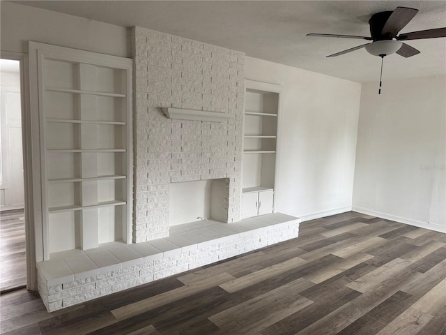 unfurnished living room with ceiling fan, wood finished floors, baseboards, built in features, and a brick fireplace