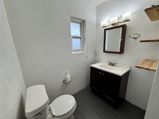 bathroom with toilet, vanity, and a textured wall