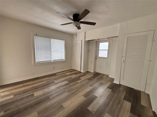 unfurnished bedroom featuring a ceiling fan, baseboards, dark wood-style flooring, and two closets