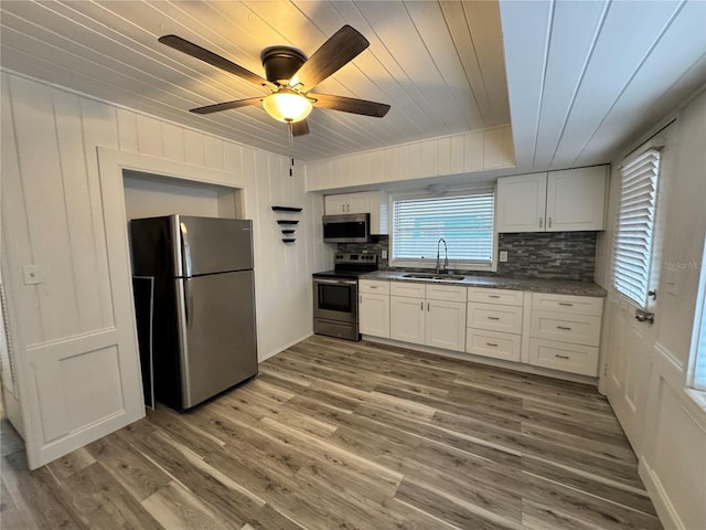 kitchen featuring light wood finished floors, tasteful backsplash, appliances with stainless steel finishes, white cabinets, and a sink