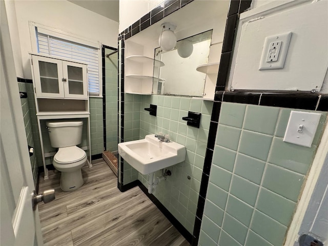 full bathroom with tile walls, toilet, a tile shower, a sink, and wood finished floors