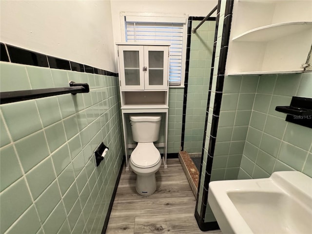 full bathroom with tile walls, toilet, a stall shower, wainscoting, and wood finished floors