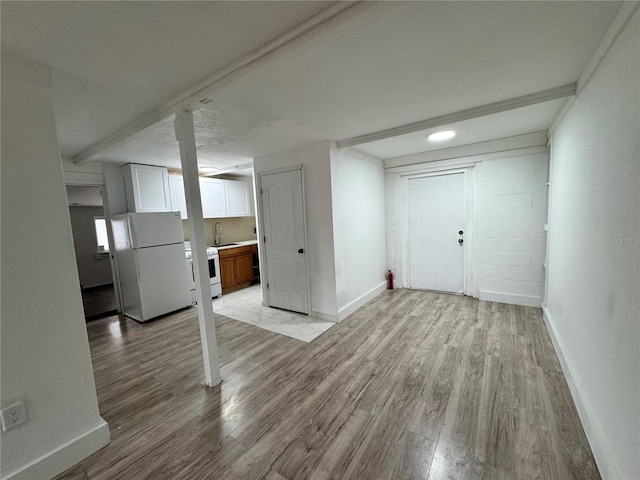 basement featuring light wood-style floors, freestanding refrigerator, a sink, and baseboards