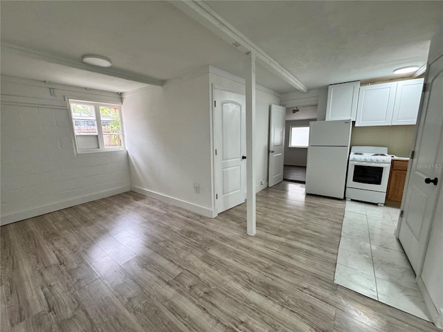 kitchen with concrete block wall, white appliances, baseboards, light wood-style flooring, and light countertops