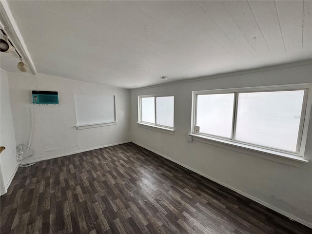 empty room featuring a wall mounted AC, dark wood finished floors, and baseboards