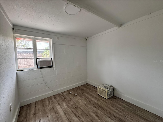 empty room with concrete block wall, baseboards, cooling unit, and wood finished floors