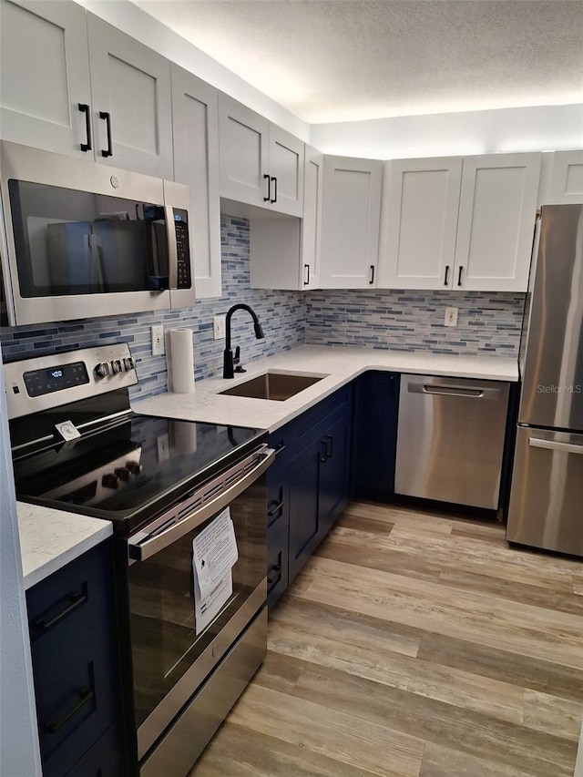 kitchen with stainless steel appliances, light wood finished floors, a sink, and tasteful backsplash