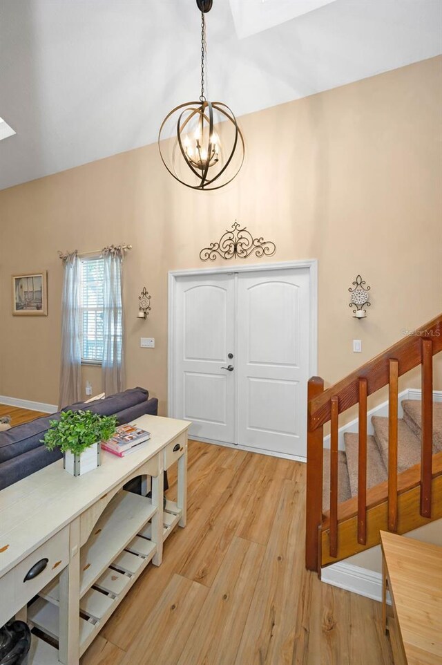 foyer entrance featuring baseboards, light wood-style flooring, stairs, lofted ceiling with skylight, and a notable chandelier